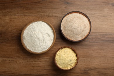 Photo of Different types of flours in bowls on wooden table, flat lay