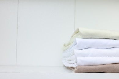 Photo of Stack of different folded shirts on white shelf, space for text. Organizing clothes