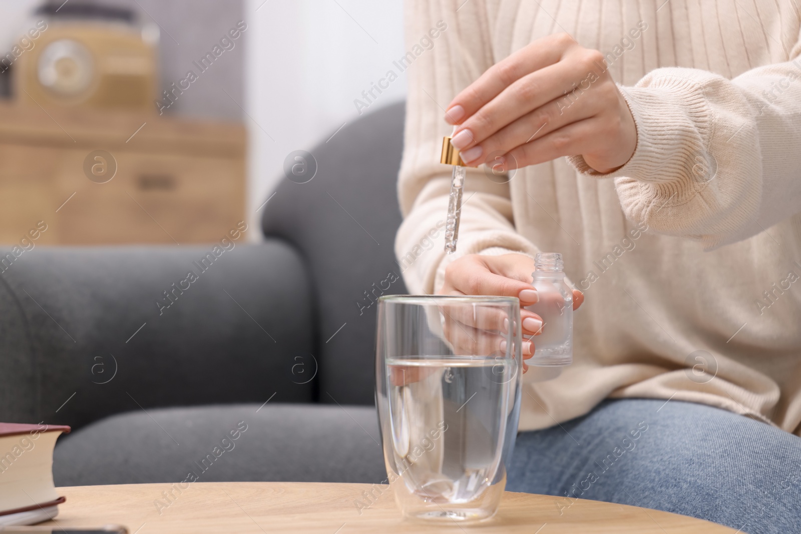 Photo of Woman dripping food supplement into glass of water on wooden table indoors, closeup. Space for text