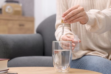 Photo of Woman dripping food supplement into glass of water on wooden table indoors, closeup. Space for text