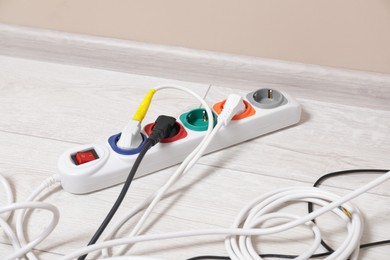 Photo of Power strip with different electrical plugs on white floor indoors
