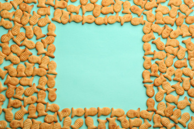 Photo of Frame of delicious goldfish crackers on turquoise background, flat lay. Space for text