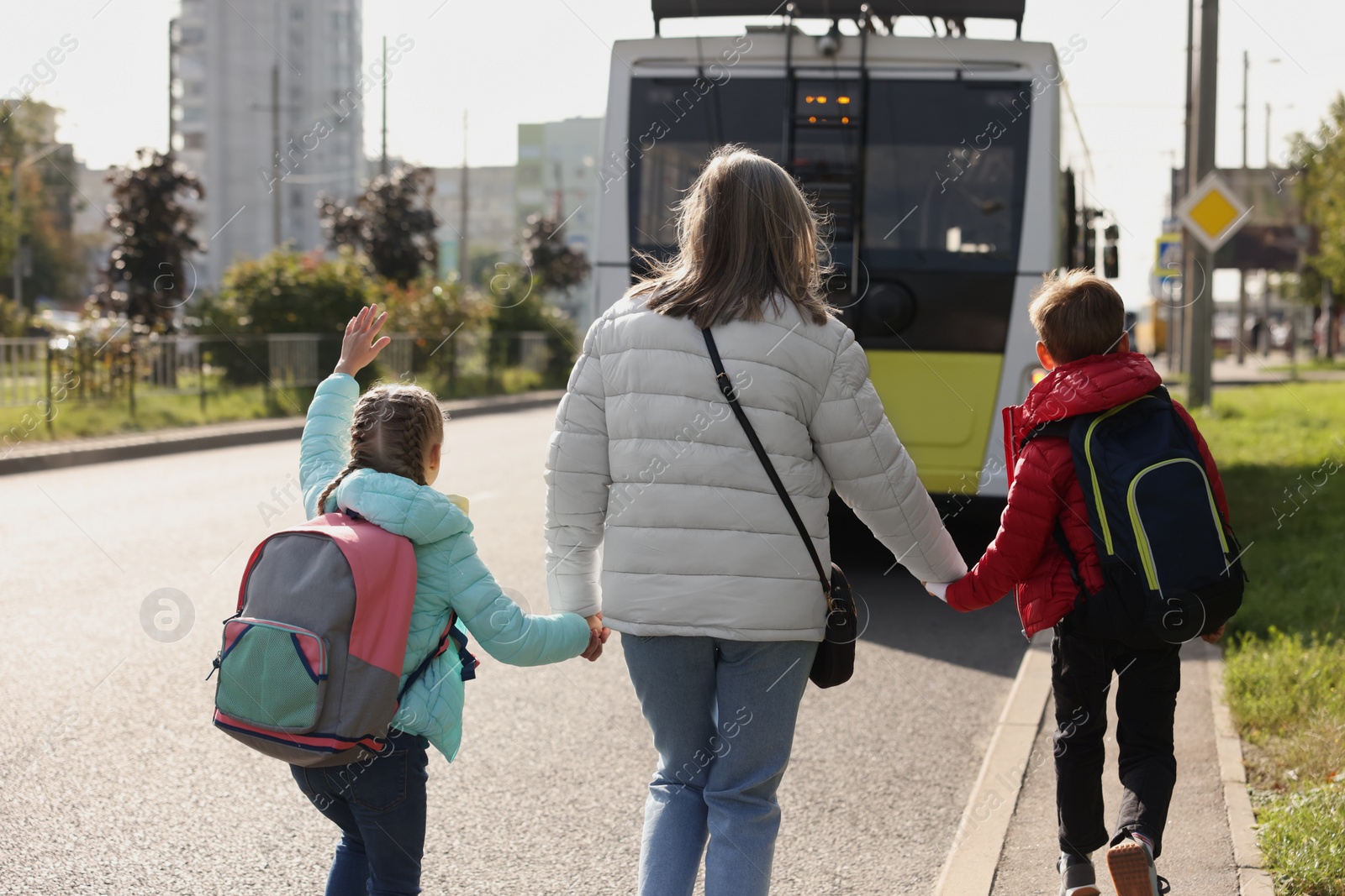 Photo of Being late for school. Senior woman and her grandchildren with backpacks running towards bus outdoors, back view