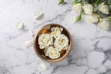 Photo of Tibetan singing bowl with water and beautiful roses on white marble table, top view