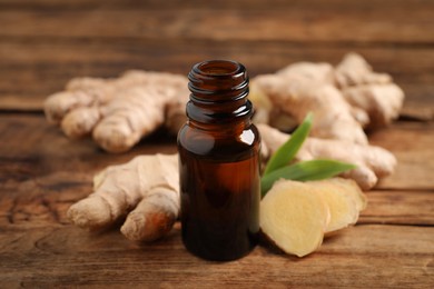 Glass bottle of essential oil and ginger root on wooden table