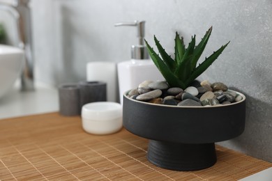 Potted artificial plant, liquid soap, decor and bamboo mat on bathroom vanity