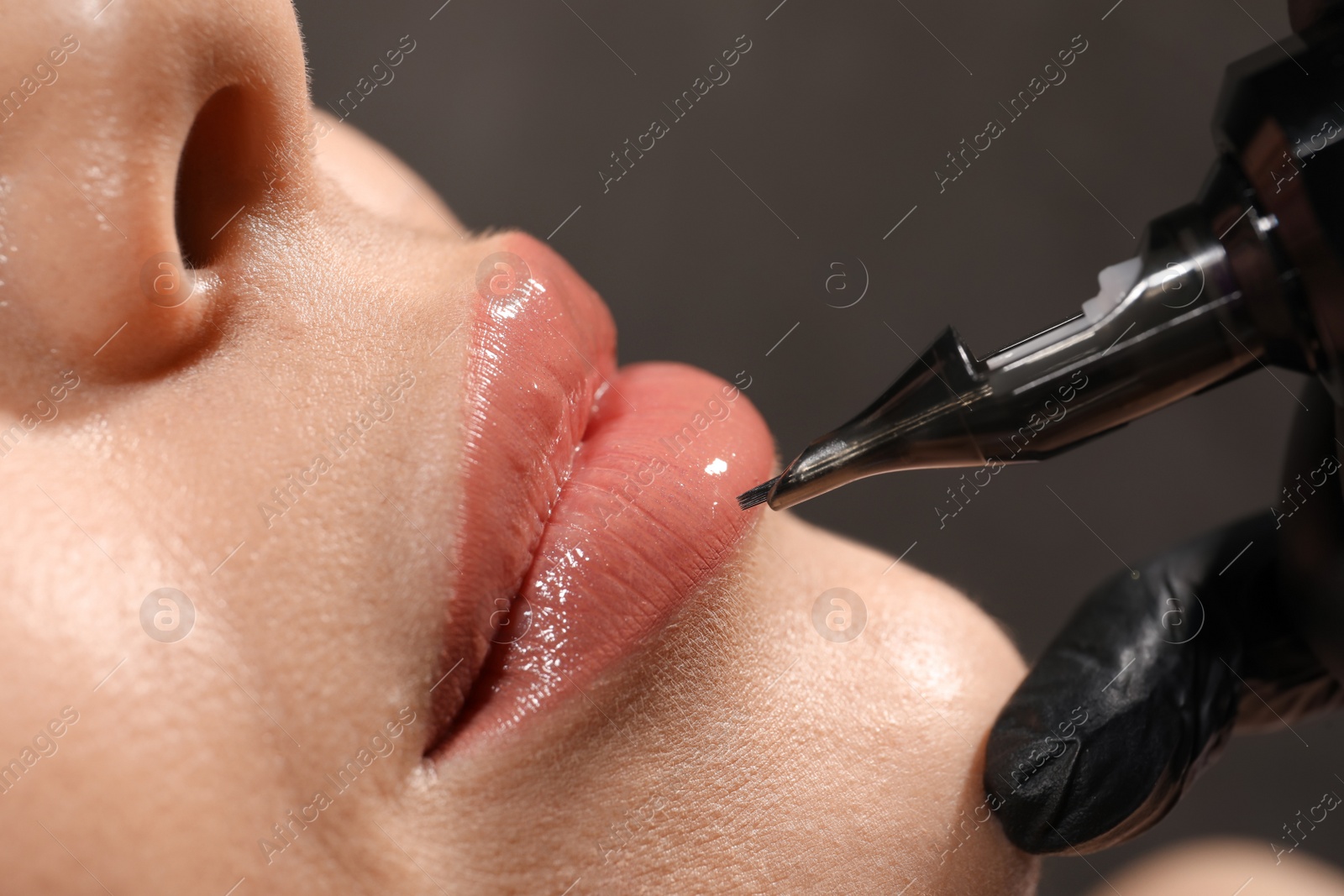 Photo of Young woman undergoing procedure of permanent lip makeup in tattoo salon, closeup