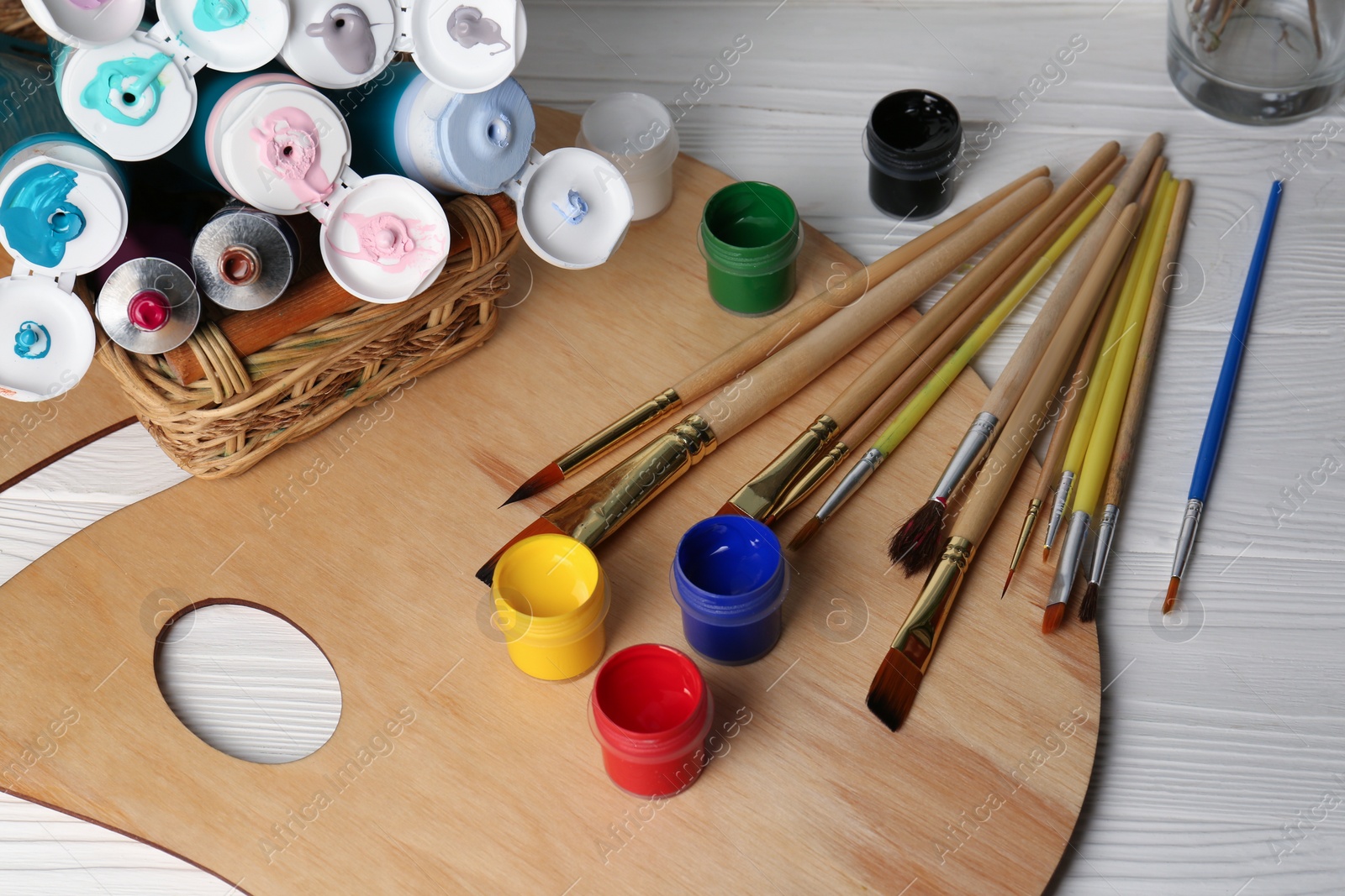 Photo of Artist's palette, colorful paints and brushes on white wooden table