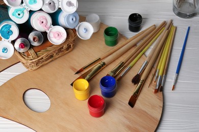Photo of Artist's palette, colorful paints and brushes on white wooden table