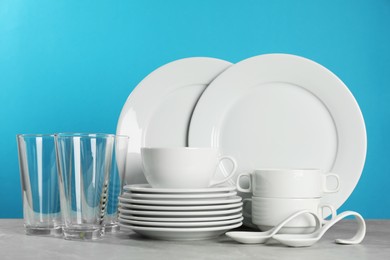Photo of Set of clean dishware and glasses on grey table against light blue background