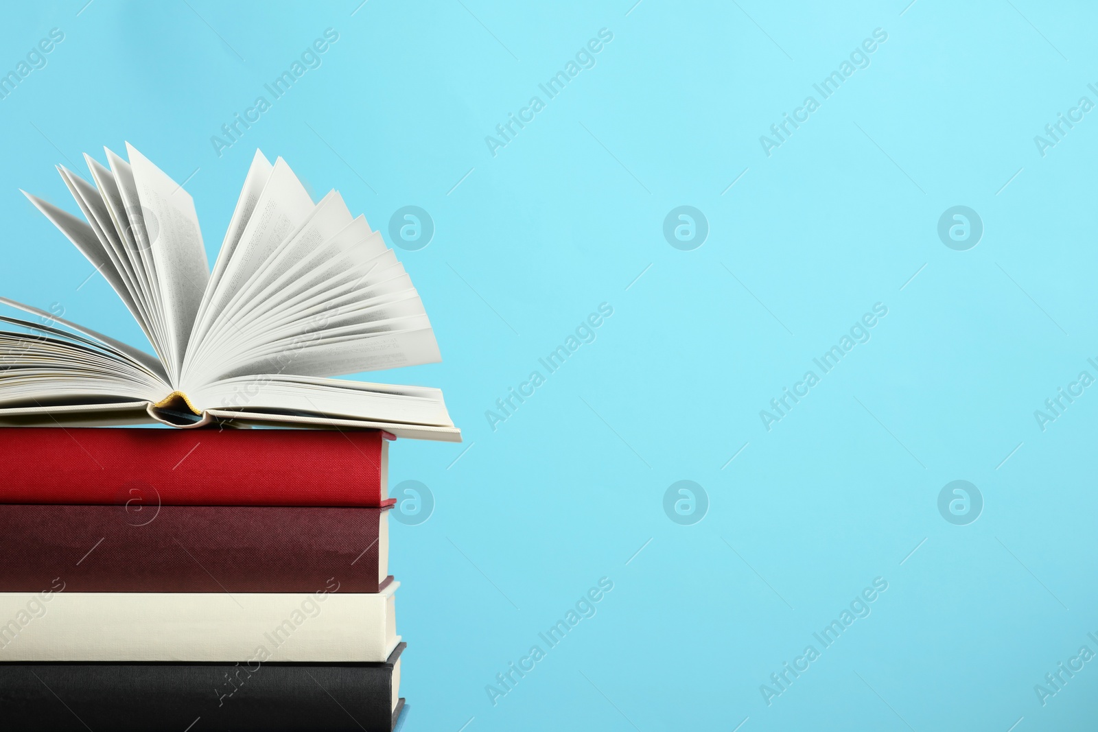 Photo of Stack of hardcover books on light blue background, space for text