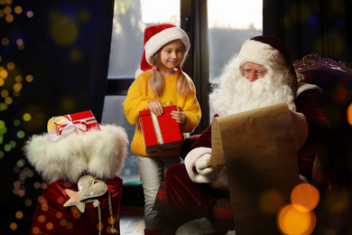 Photo of Little girl with Christmas gift near Santa Claus indoors