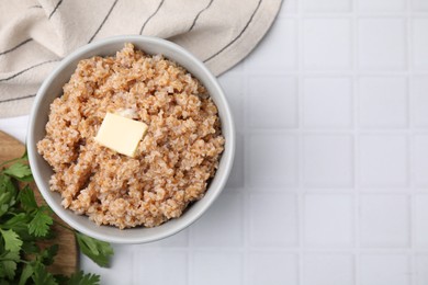 Tasty wheat porridge with parsley and butter on white tiled table, top view. Space for text