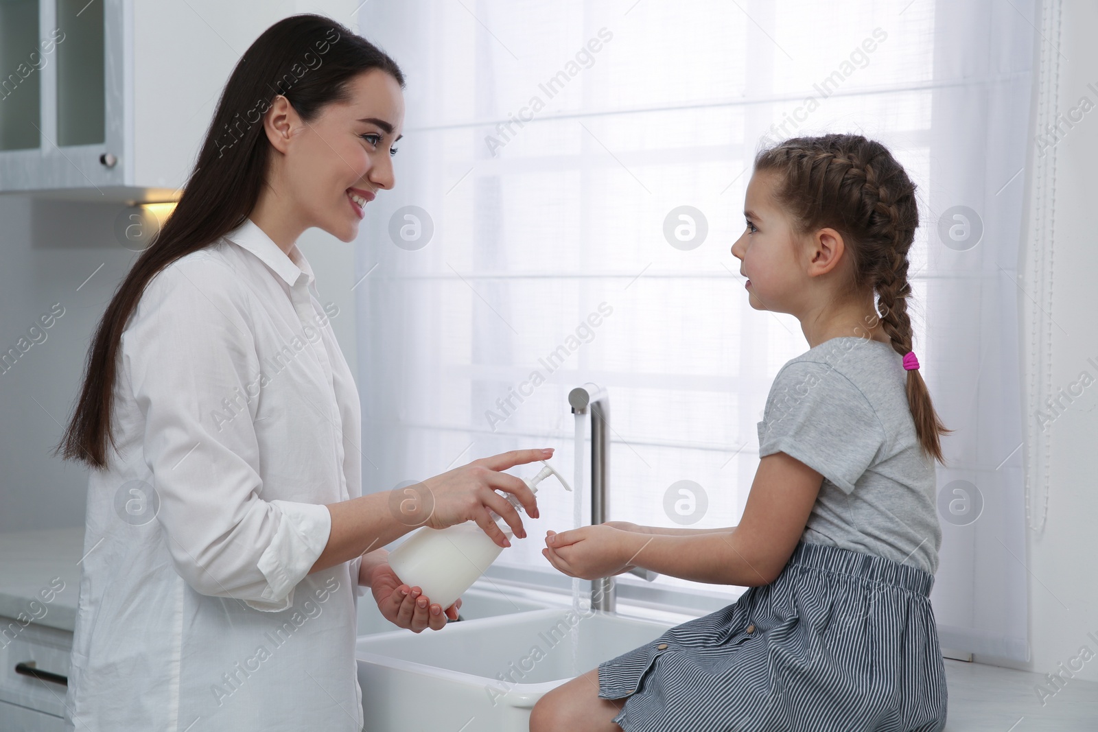 Photo of Mother and daughter washing hands with liquid soap together in kitchen