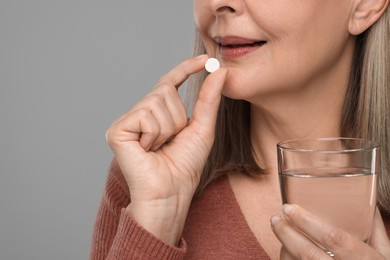 Photo of Senior woman with glass of water taking pill on grey background, closeup