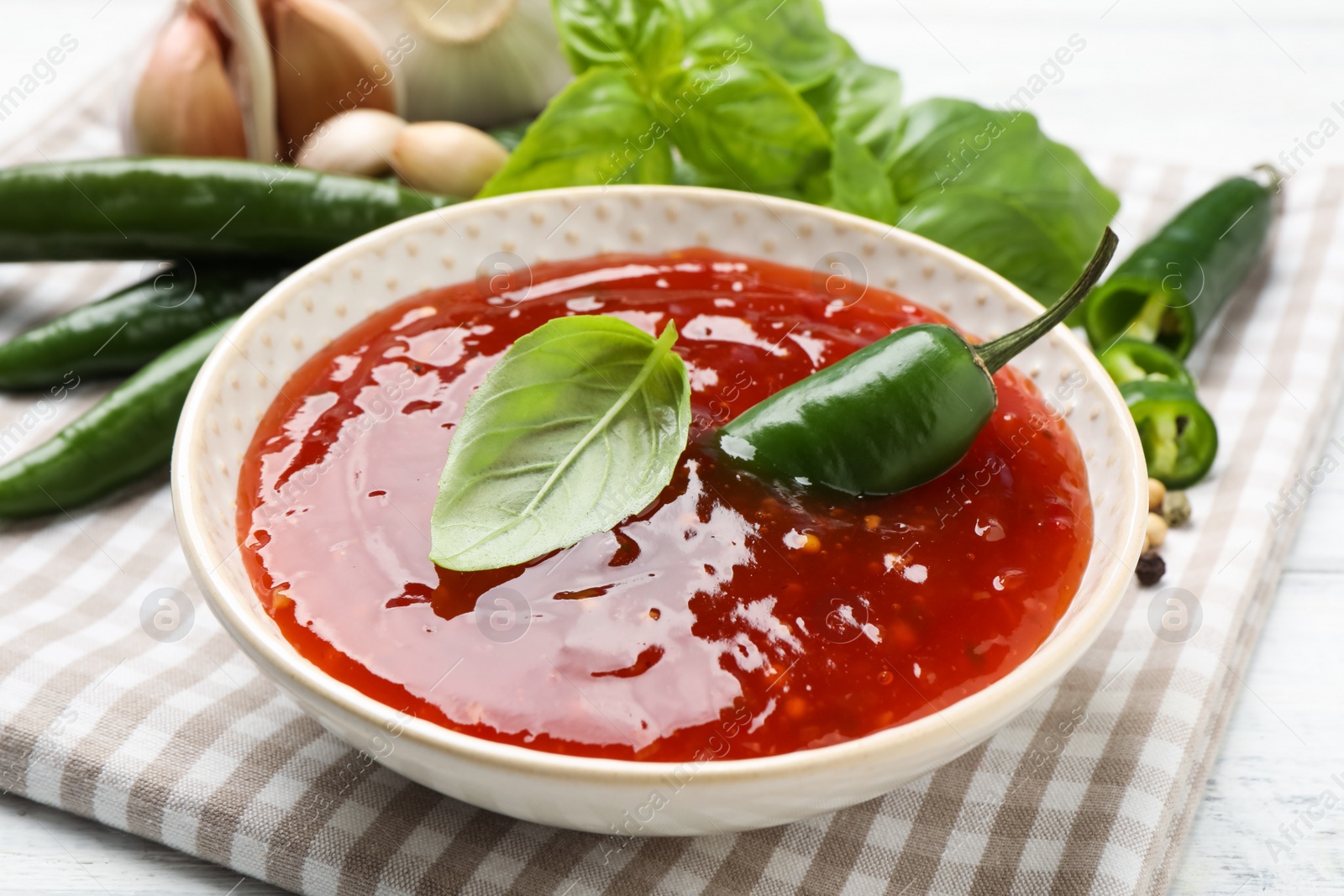 Photo of Spicy chili sauce with basil on white table