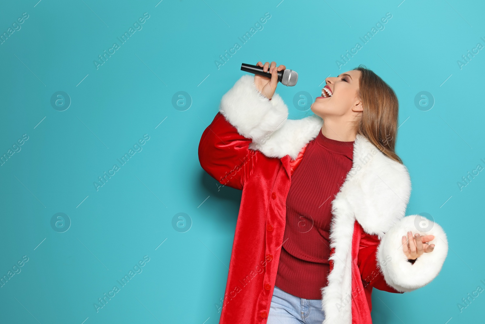 Photo of Young woman in Santa costume singing into microphone on color background. Christmas music