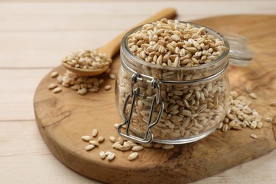 Dry pearl barley in glass jar and spoon on light wooden table, closeup