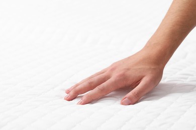Man touching soft mattress, closeup. Space for text