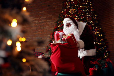 Santa Claus packing gifts into bag near Christmas tree