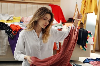 Photo of Young woman with dress in messy room. Fast fashion concept