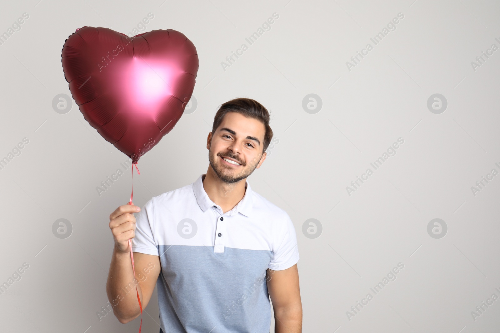 Photo of Portrait of young man with heart shaped balloon on light background. Space for text