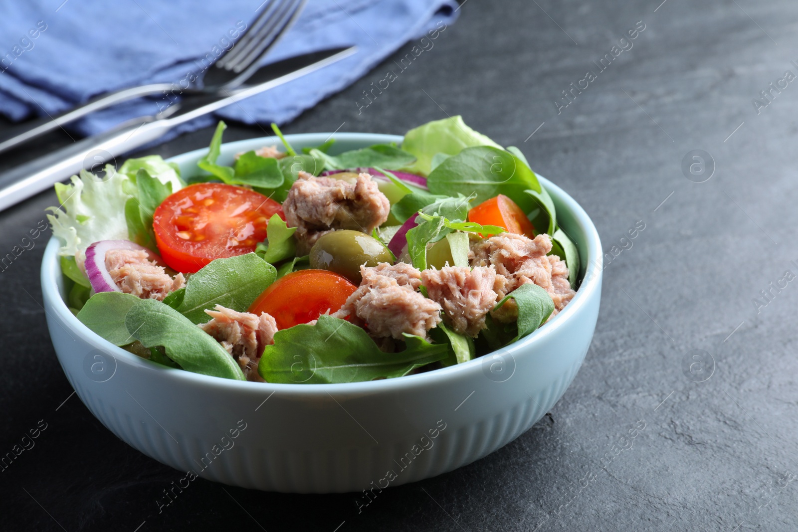 Photo of Bowl of delicious salad with canned tuna and vegetables on black table