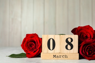 Photo of Wooden block calendar with date 8th of March and roses on table against light background, space for text. International Women's Day