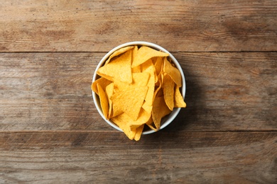 Photo of Tasty mexican nachos chips in bowl on wooden table, top view