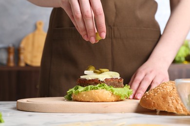 Photo of Woman making delicious vegetarian burger at white marble table, closeup