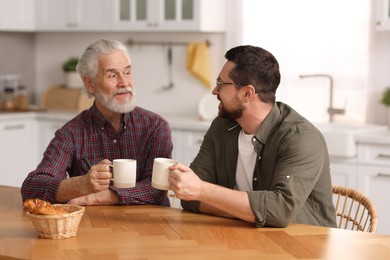 Photo of Happy son and his dad with cups talking in kitchen