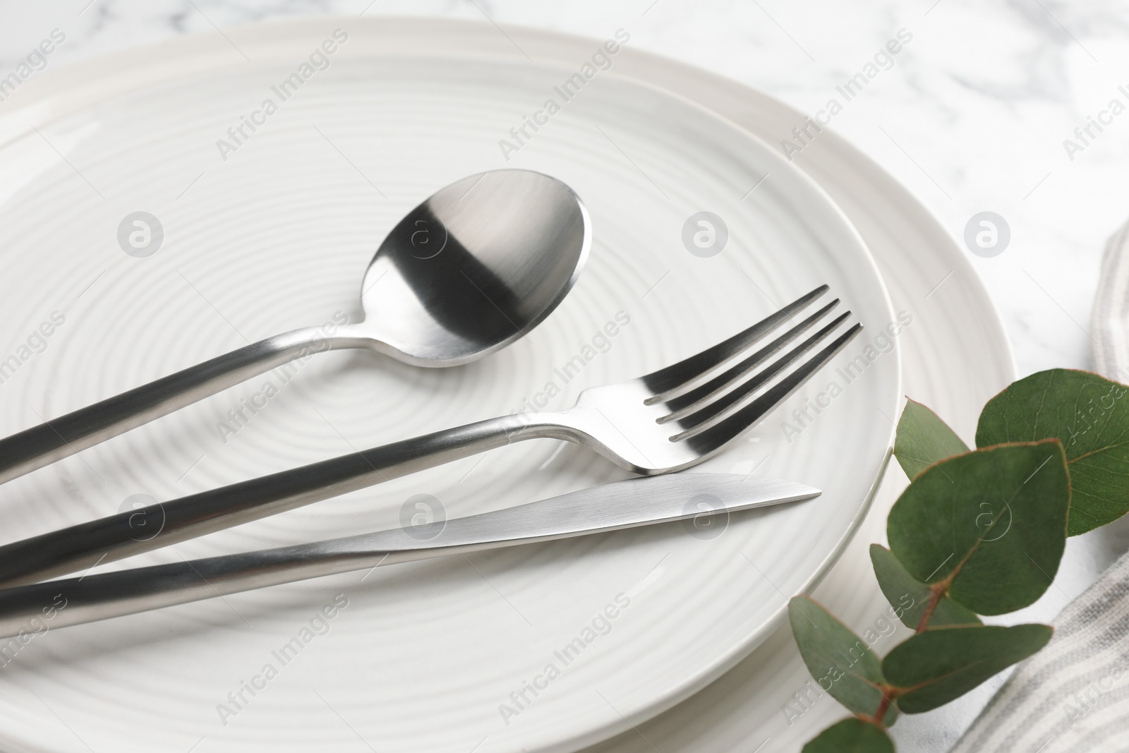 Photo of Stylish setting with cutlery, eucalyptus branch and plates on table, closeup