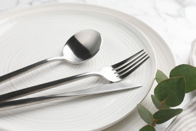 Stylish setting with cutlery, eucalyptus branch and plates on table, closeup