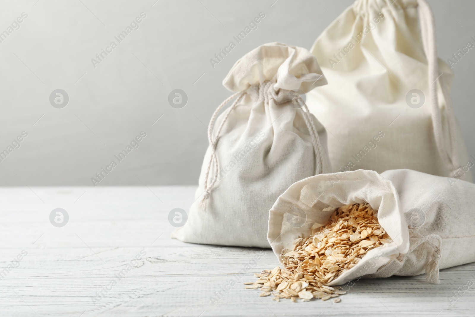 Photo of Cotton eco bags with oat flakes on white wooden table. Space for text