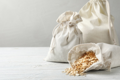 Photo of Cotton eco bags with oat flakes on white wooden table. Space for text