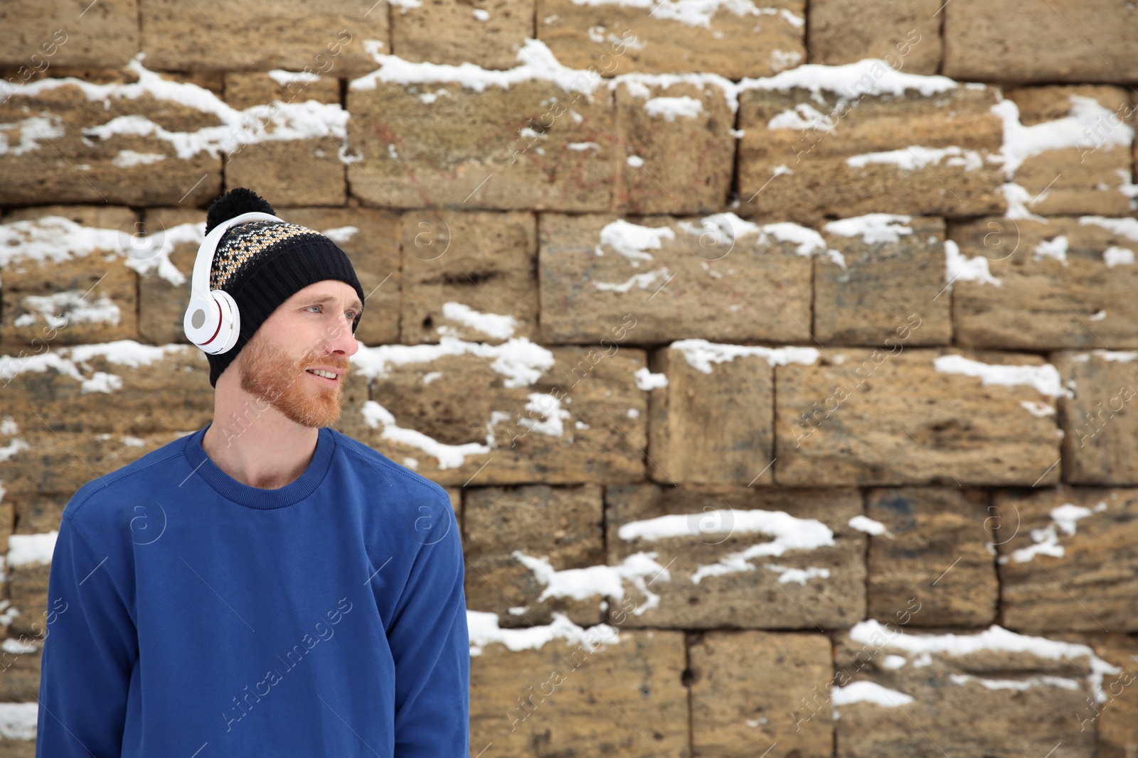 Photo of Young man listening to music with headphones against stone wall. Space for text