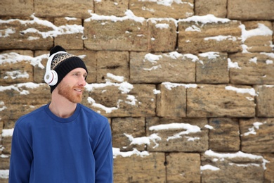 Young man listening to music with headphones against stone wall. Space for text