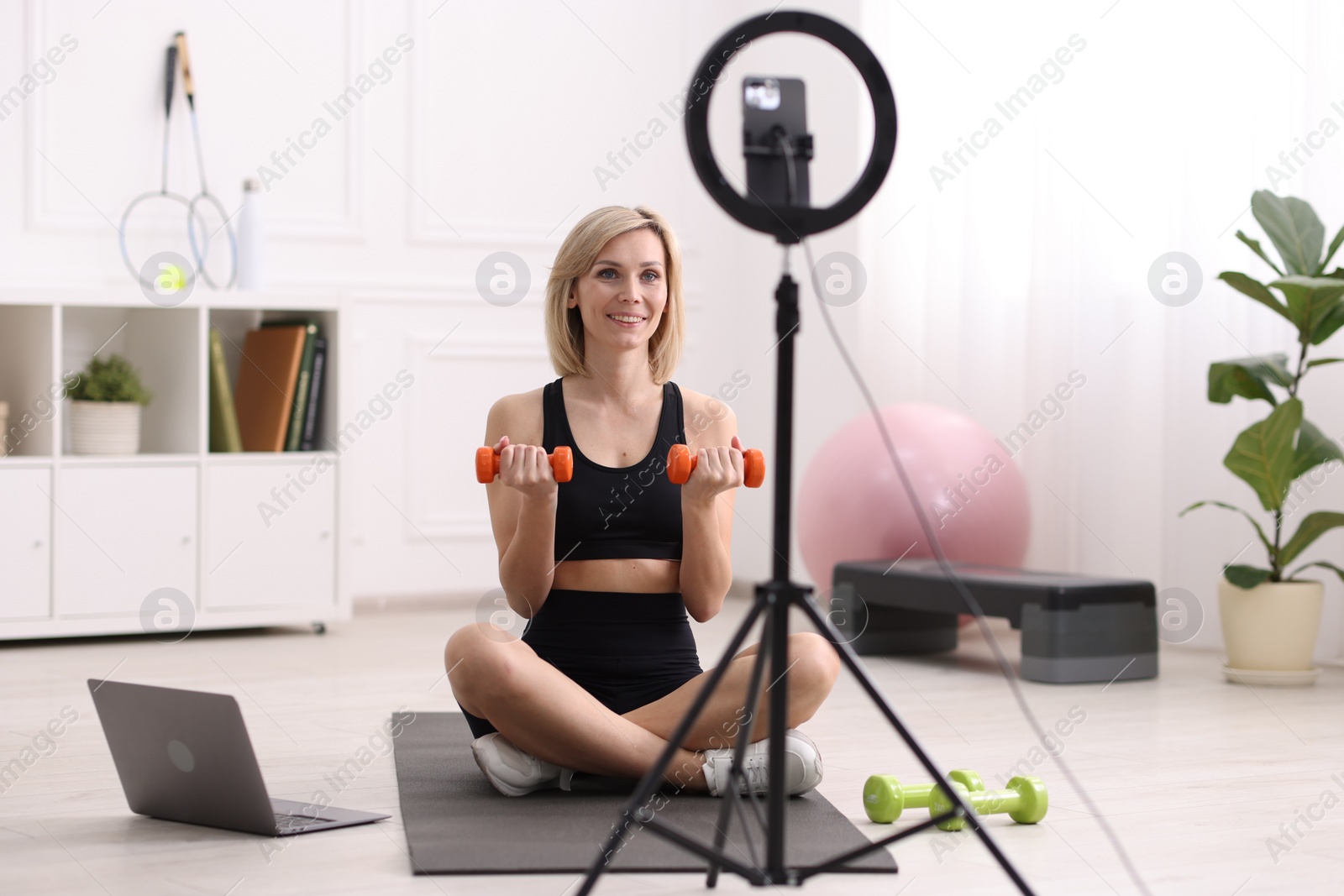 Photo of Smiling sports blogger working out with dumbbells while streaming online fitness lesson at home