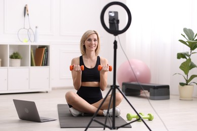 Smiling sports blogger working out with dumbbells while streaming online fitness lesson at home