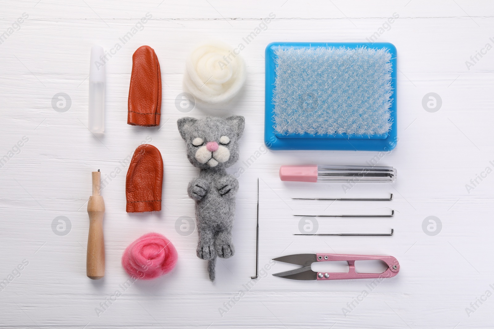 Photo of Felted cat, wool and different tools on white wooden table, flat lay