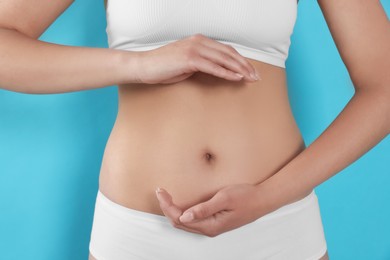 Photo of Woman in underwear holding something near her belly on light blue background, closeup. Healthy stomach