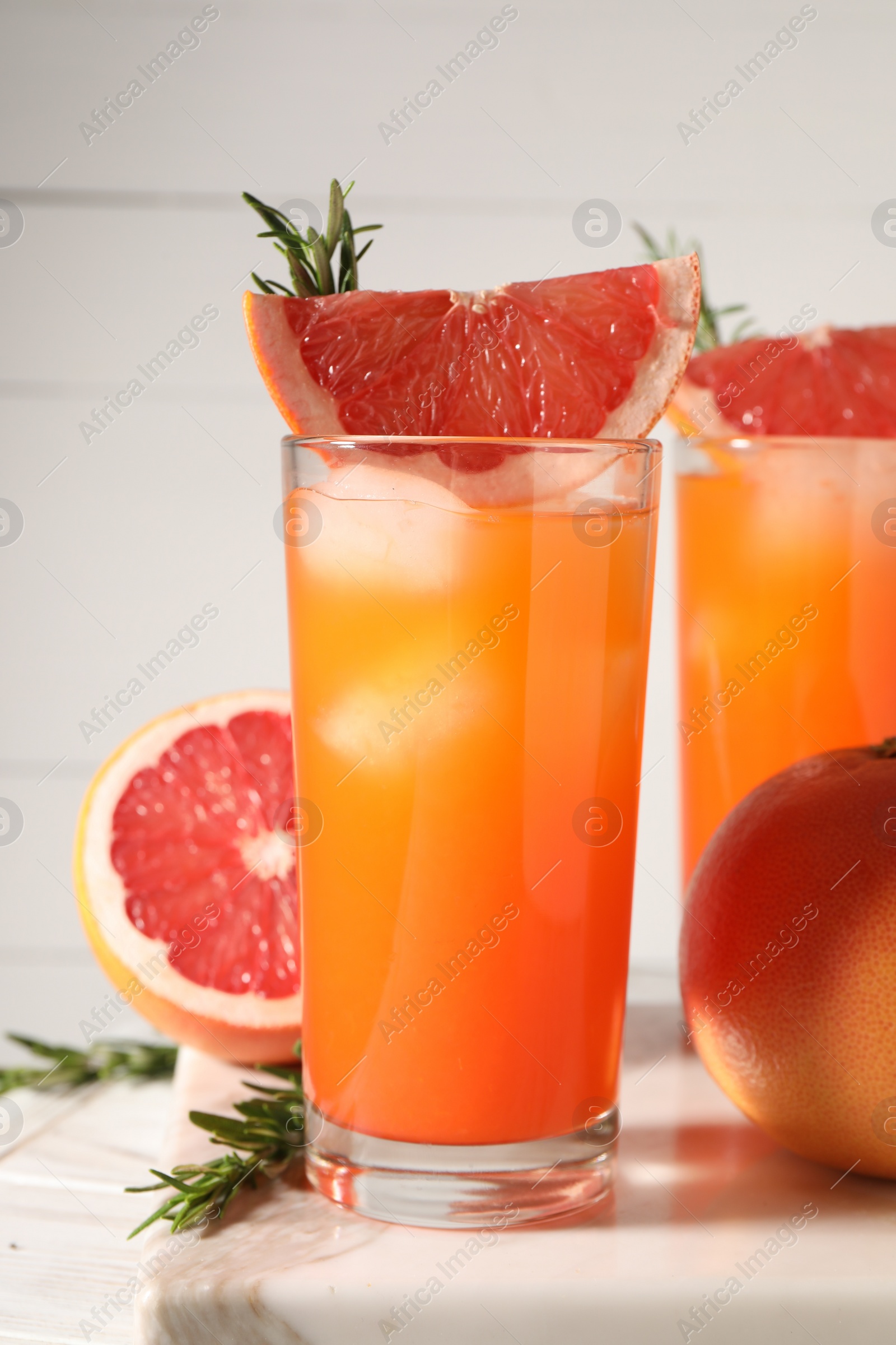 Photo of Tasty grapefruit drink with ice in glasses, rosemary and fresh fruits on light table