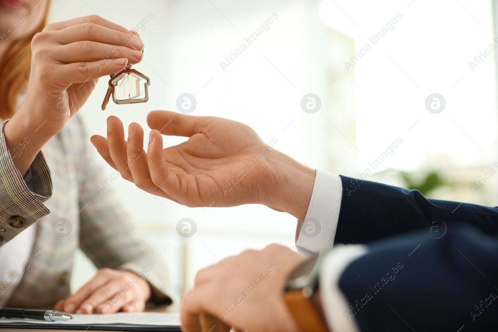 Photo of Real estate agent giving key with trinket to client in office, closeup