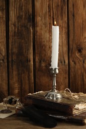 Elegant candlestick with burning candle and ancient books on wooden table
