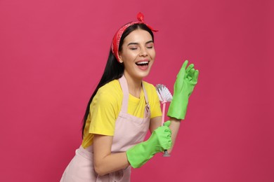 Young housewife with brush on pink background