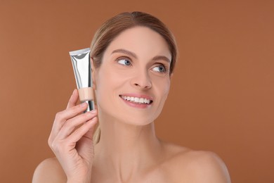 Photo of Woman holding tube of foundation on brown background