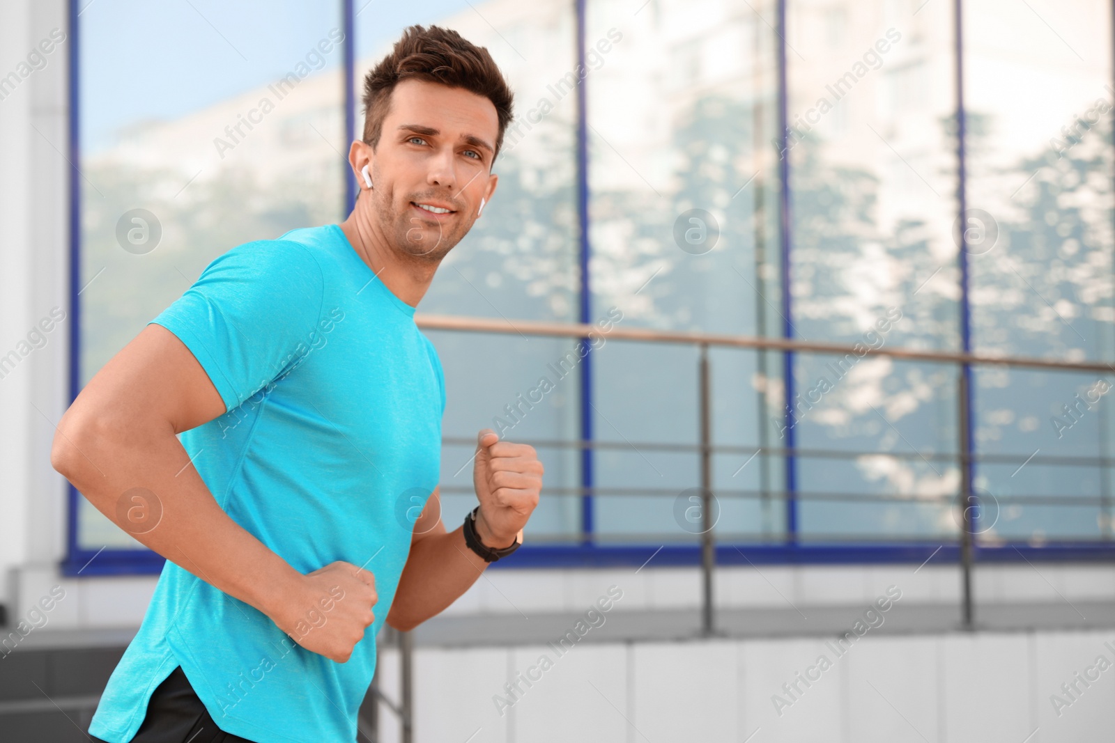 Photo of Young sportsman with wireless earphones running on city street