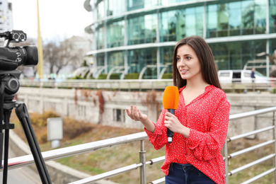 Photo of Young female journalist with microphone working on city street