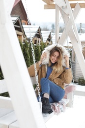 Young woman in warm clothes resting on outdoor swing. Winter vacation