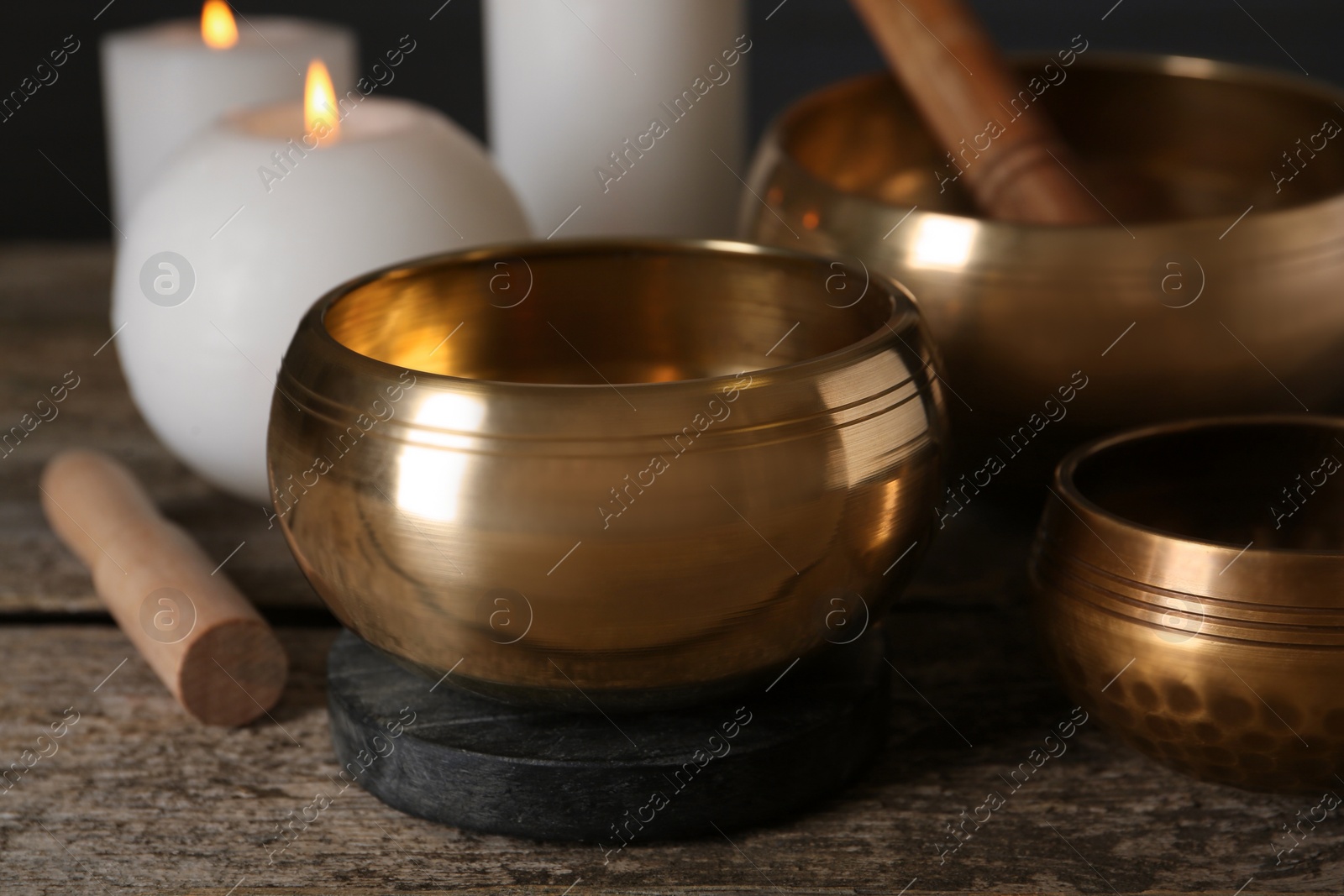 Photo of Golden singing bowls, mallets and burning candles on wooden table, closeup